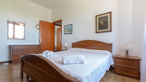 Ein ordentlich eingerichtetes Schlafzimmer mit einem hölzernen Bett, einem Nachttisch mit Lampe, einer Kommode und einem gerahmten Bild an der Wand.