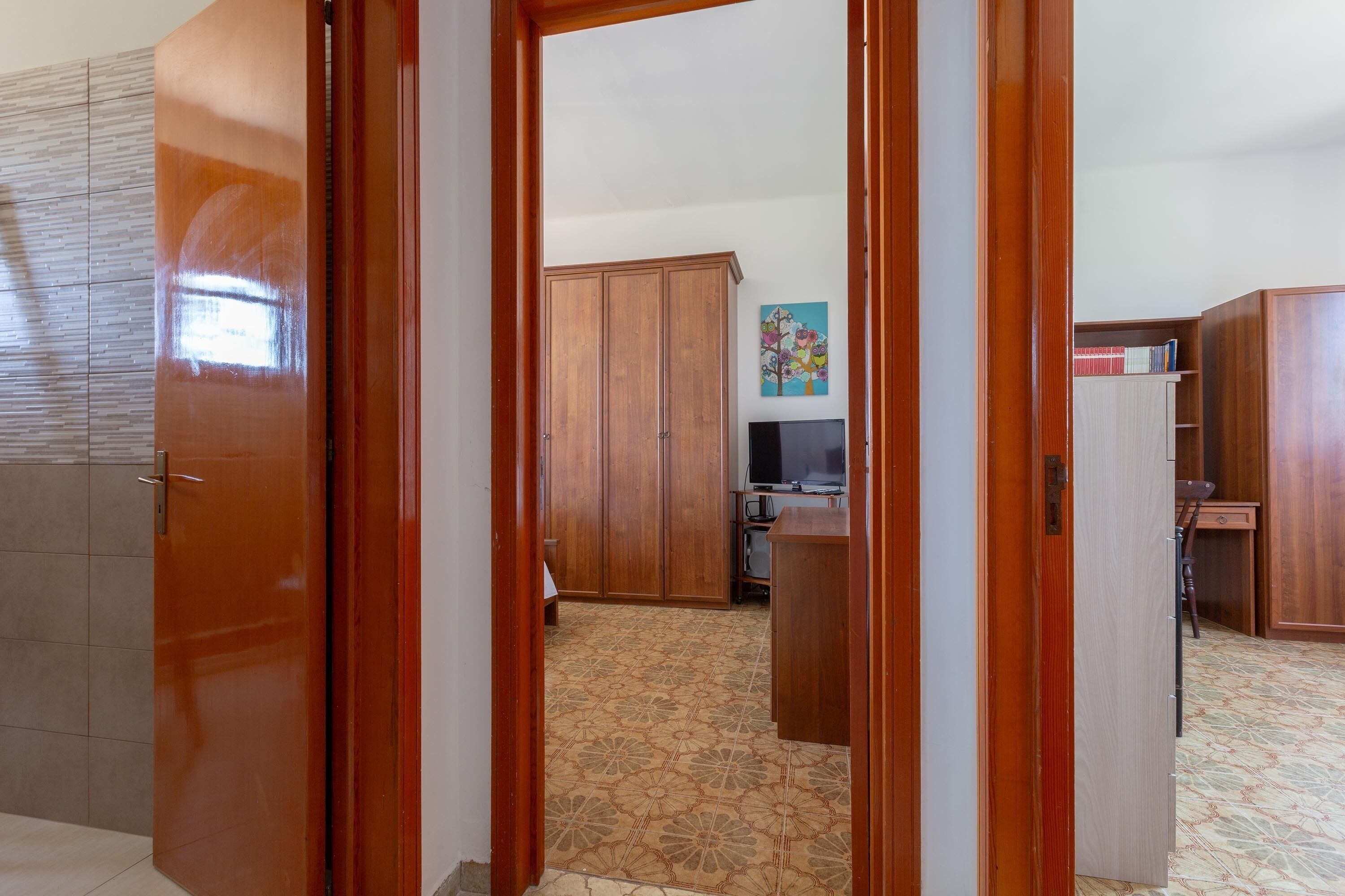 A room with a wooden wardrobe, a desk, and a television.