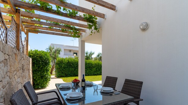 Ein Essbereich im Freien mit einem Glastisch, Korbstühlen und einer mit Weinreben bewachsenen Pergola.