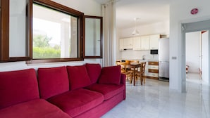 Ein modernes Wohnzimmer mit einem roten Sofa, einer Essecke mit Holzmöbeln und einer Küche mit weißen Schränken und einem Kühlschrank.