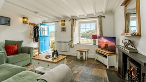A cozy living room with a fireplace, a television, and a view of the outdoors through a window. - Fal River Cottage (Truro)