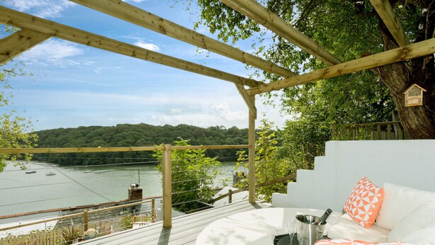 A wooden deck with a white outdoor sofa, a metal bucket, and a wooden birdhouse. - Fal River Cottage (Truro)