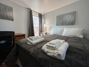 Ein Hotelzimmer mit einem Bett, zwei Kissen, einem Schreibtisch, einem Sessel, einer Lampe und Bildern an den Wänden.
