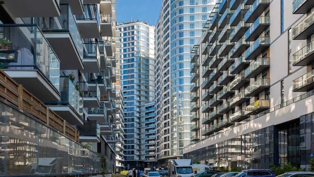 Uma rua urbana moderna com edifícios residenciais altos, céu claro e carros estacionados.