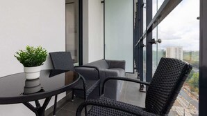 Uma varanda com uma mesa redonda, duas cadeiras, um vaso de planta e vista para um horizonte urbano.