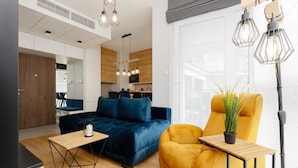 Een moderne woonkamer met een donkerblauwe bank, een gele fauteuil en een houten salontafel.