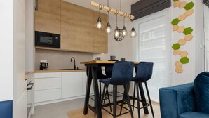 Een moderne keuken met houten kastjes, een zwarte magnetron en een houten eettafel met twee blauwe stoelen.