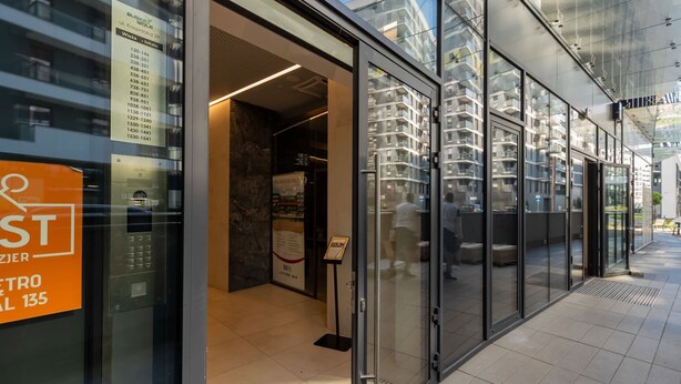 Een modern gebouw met een glazen gevel, een zichtbare lift en een bord dat een metrostation aangeeft.