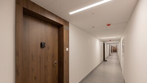 Een gang met een houten deur met het nummer 713, verlichte plafond en een betegelde vloer.