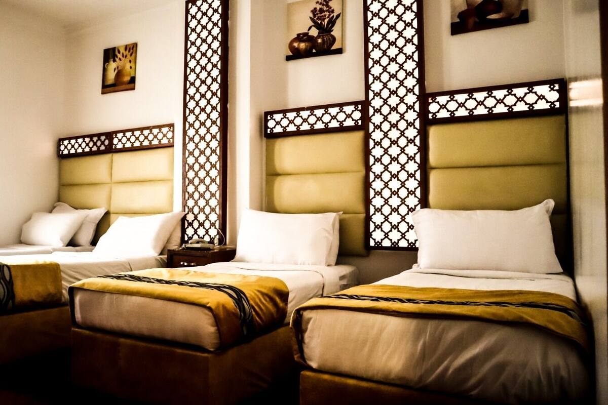 A hotel room with three beds, each with a headboard and pillows.