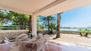 An outdoor dining area with a table set for four, surrounded by white chairs, overlooking a beach and a body of water. - 3563 Villa del Bacino - App Rosso by Barbarhouse (Porto Cesareo)