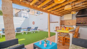 Un patio al aire libre con una mesa de comedor, sillas, y una mesita con adornos. Se observan sillones de descanso y una piscina al fondo.