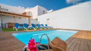 Area della piscina con poltrona relax, un molo in legno e un edificio bianco sullo sfondo.