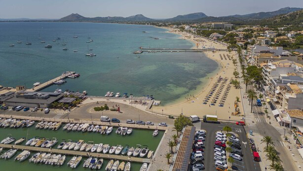 Una cittadina costiera con un porto turistico, spiaggia e edifici residenziali.