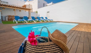 A poolside area with lounge chairs, a wooden deck, and a white building in the background.
