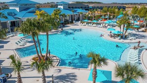 Una gran piscina al aire libre rodeada de palmeras y sillas de descanso, con vistas a edificios de hotel al fondo.