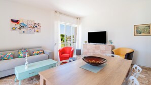 A modern living room with a sofa, a dining table, a red chair, and a TV. - 3564 Villa del Bacino - App Blu by Barbarhouse (Porto Cesareo)