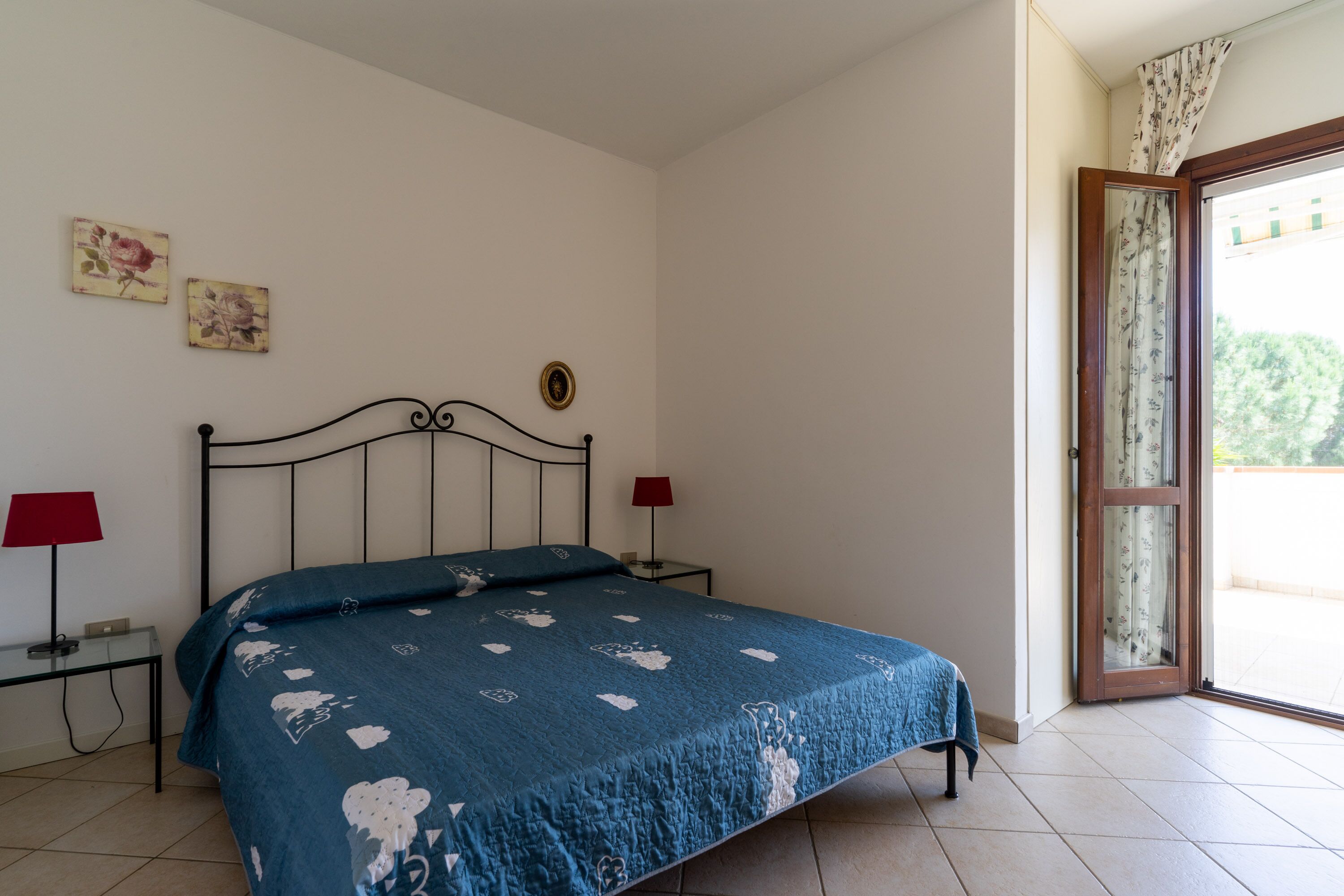 A bedroom with a bed, two bedside lamps, a small table, and a window with a view.