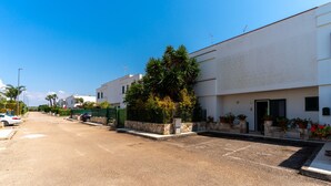 A residential street with white houses, a green fence, and a parking area. - 3441 Villa Selvaggia by Barbarhouse (Nardò)