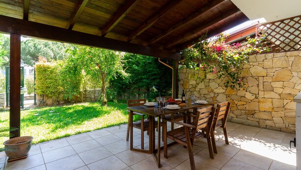 An outdoor patio with a stone wall, wooden table, and chairs. - 3441 Villa Selvaggia by Barbarhouse (Nardò)