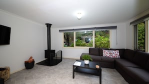 A living room with a black wood stove, a sofa, a coffee table, and a window with a view of greenery. - Rose Cottage - Nannup (Nannup)