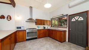 A kitchen with wooden cabinets, a stove, a microwave, and a window with a view of greenery. - Rose Cottage - Nannup (Nannup)