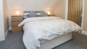 A bedroom with a bed, two bedside tables, a nightstand, and a wooden door. - Spicery Barn Loft (Exeter)