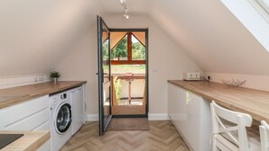 A compact kitchen with a washing machine, wooden countertops, and a view through an open door to an outdoor area. - Spicery Barn Loft (Exeter)