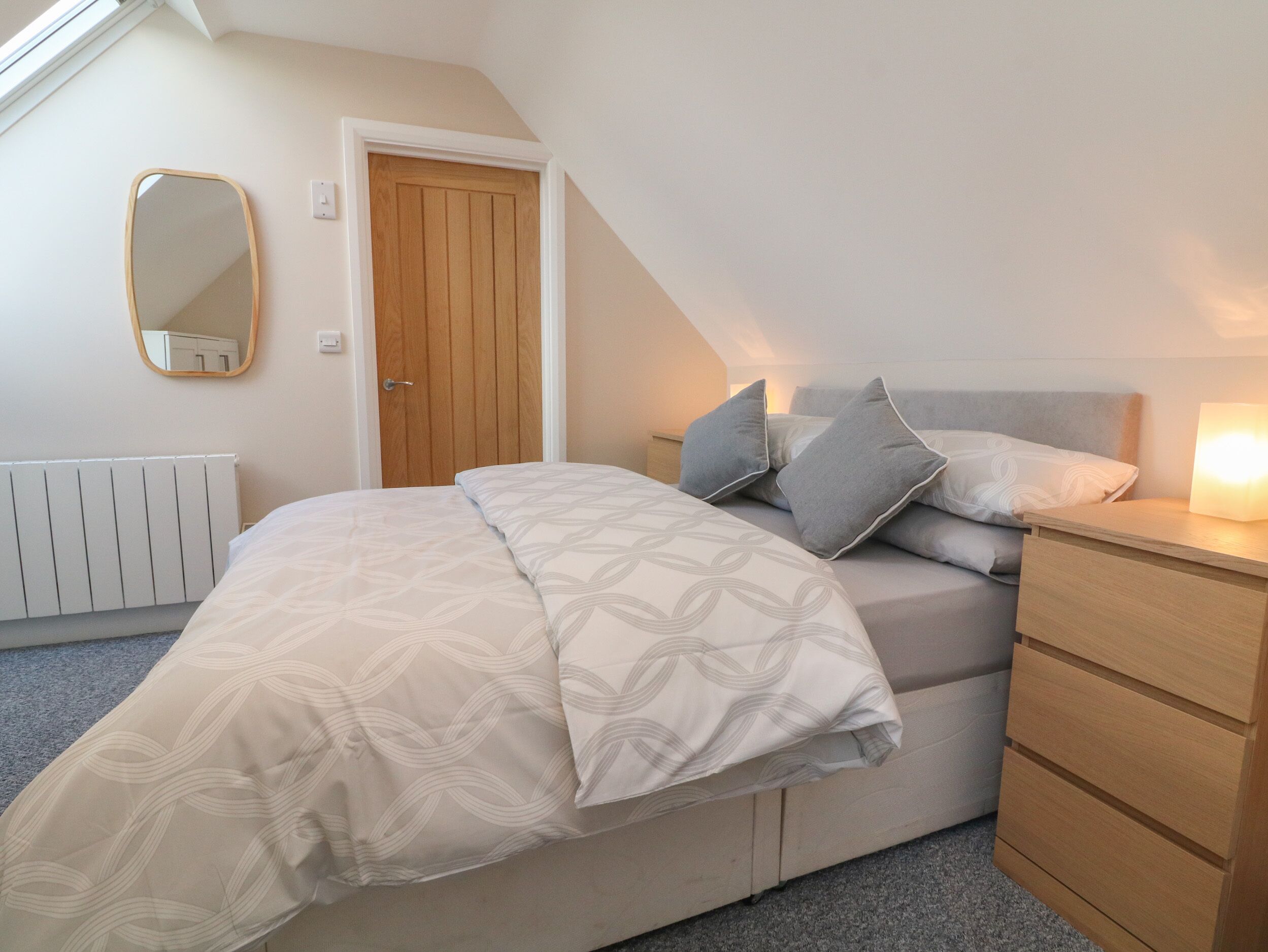 A bedroom with a bed, a dresser, a nightstand, a mirror, and a door.