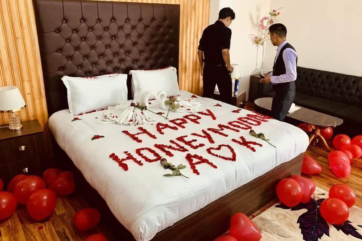 Habitación de hotel con una cama decorada con el mensaje 'Happy Honeymoon AOK', rodeada de globos rojos.