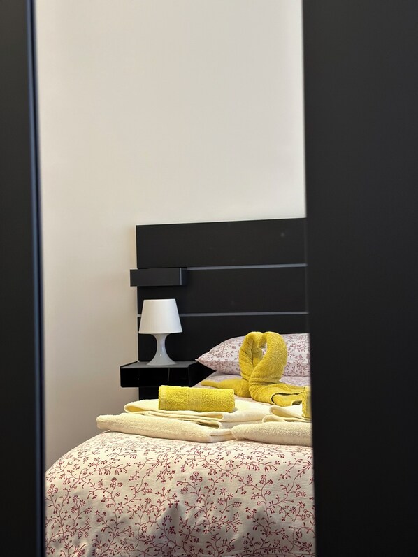 A neatly made bed with yellow towels, a white lamp, and a floral-patterned pillow on a black headboard.