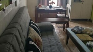 Una sala de estar con sofá, una mesa de comedor lista para cuatro personas y una cocina con armarios y refrigerador.