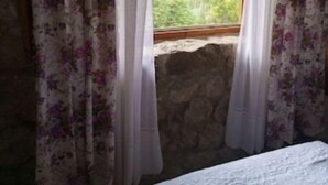 Una habitación con cama, cortinas florales y vistas al verdor a través de una ventana.