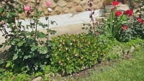 Un edificio con fachada blanca, base de piedra y un pequeño balcón con flores rosadas.
