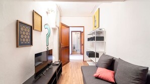 A modern living room with a flat-screen TV, a grey sofa with a red pillow, a wooden floor, and a hallway leading to another room. - Central and cozy loft with courtyard (Bologna)