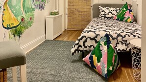 Ein Schlafzimmer mit Bett, Stuhl, kleinem Tisch, Wandbild und einer Tür.