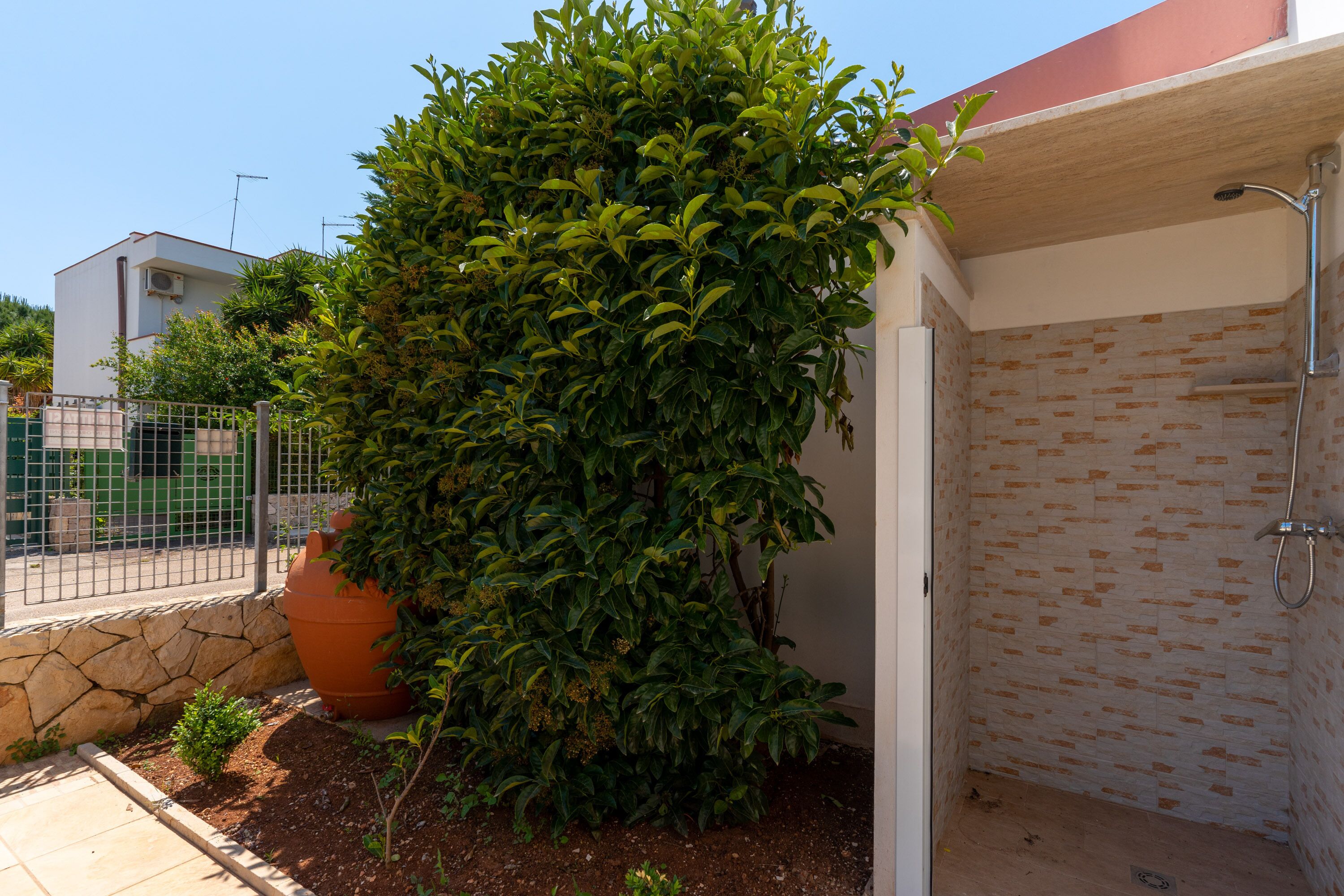 Un petit espace de douche extérieur, à l’abri, avec un mur carrelé et une pomme de douche en métal.