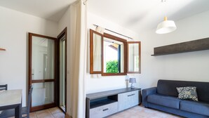 Ein modernes Wohnzimmer mit einer Couch, einem Esstisch mit Stühlen, einer TV-Konsole und einer Glastür zum Balkon.