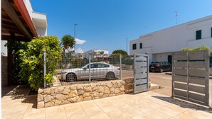 Ein ausgewiesener Parkbereich mit Steinmauer und Metallzaun, ein geparktes Auto und ein Gebäude mit flachem Dach und weißer Fassade.