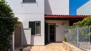 Ein modernes Haus mit einer Steinwand, einer gefliesten Terrasse und einem Metallzaun.