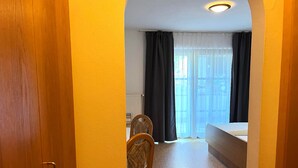 A narrow hallway leading to a bedroom with a bed, a chair, and a window with curtains. - Landgasthof Blasini - Pfahlhof (Zandt)