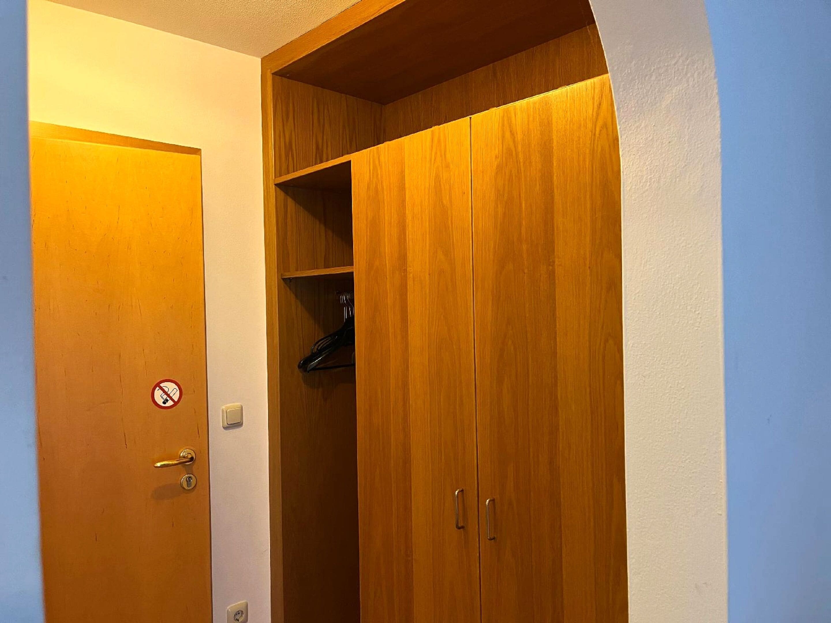 Een houten garderobe met een hanggedeelte, een deur met een rookverbodssignaal en een lichtschakelaar.