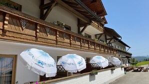 A traditional chalet with wooden balconies, outdoor seating, and umbrellas branded with a local beer. - Landgasthof Blasini - Pfahlhof (Zandt)