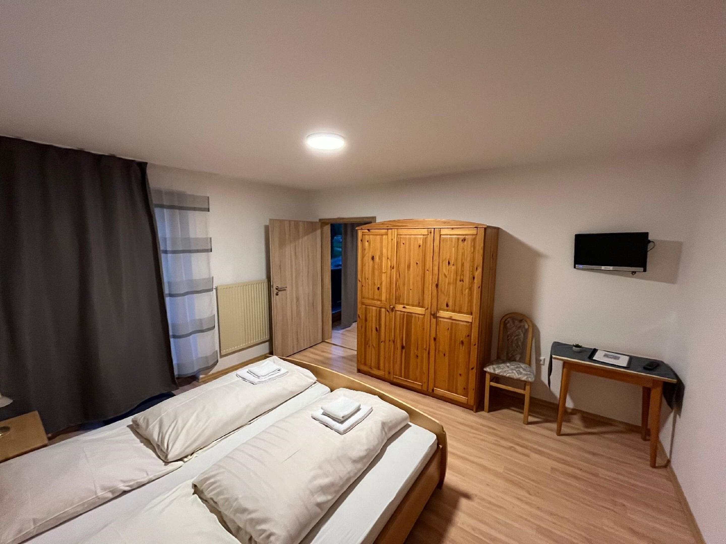 Een hotelkamer met een bed, een houten garderobe, een bureau, een stoel en een televisie.