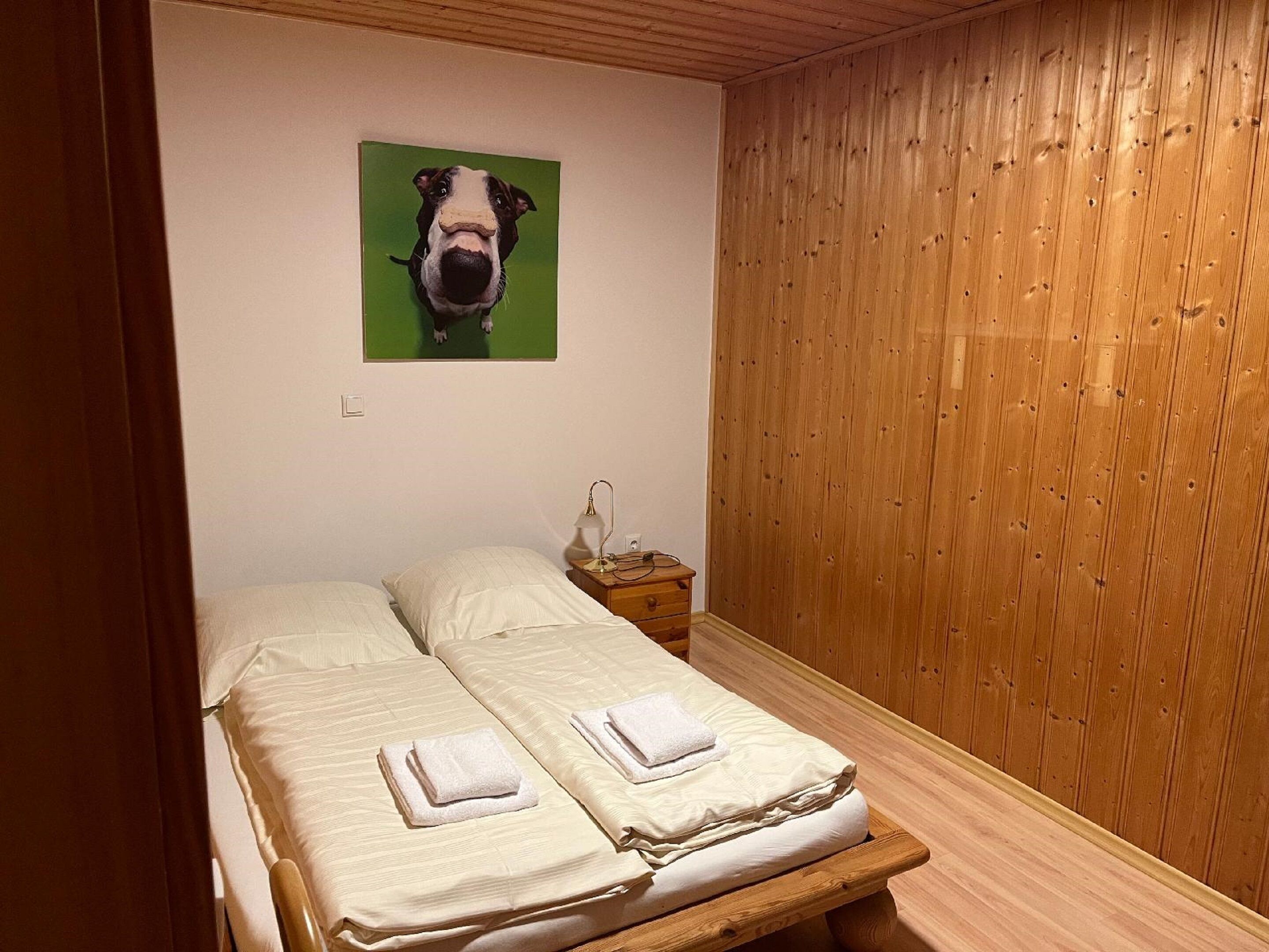 Un dormitori amb dos llits, un capçal de fusta, una tauleta de nit i una fotografia d'un gos penjada a la paret.