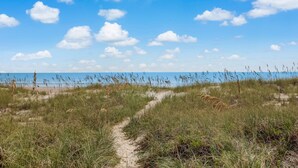 En sti af sand der fører til en strand med en klar blå himmel og spredte skyer.