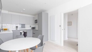 Una cocina moderna con armarios blancos, microondas y un comedor con mesa blanca y sillas grises.