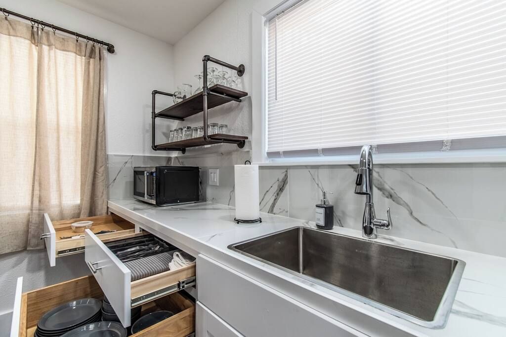 A compact kitchen with a built-in microwave, a stainless steel sink, and a shelf with glassware.