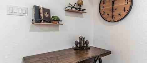 A wooden desk with a globe and books on a shelf, a large wall clock, and a power outlet.