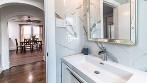 Ein modernes Badezimmer mit Marmor-Spritzschutz, einem großen Spiegel und einem weißen Waschbecken.